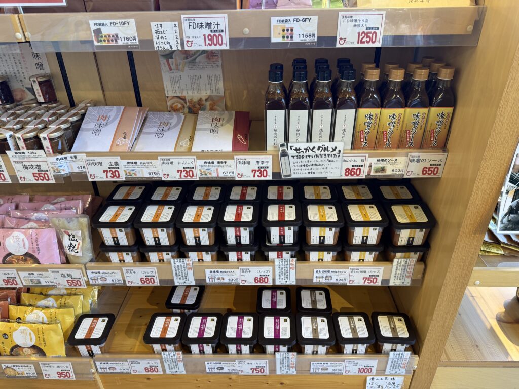 道の駅びんご府中の棚に並ぶ、カップ入りの府中味噌やボトルのタレ、インスタント味噌汁などの特産品。
