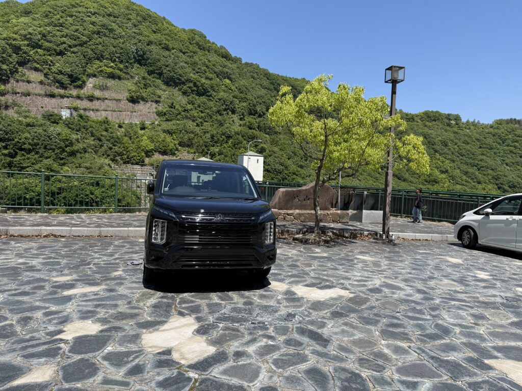 四川ダムの駐車場に停まる黒い三菱デリカD:5と、背景に広がる緑豊かな山。